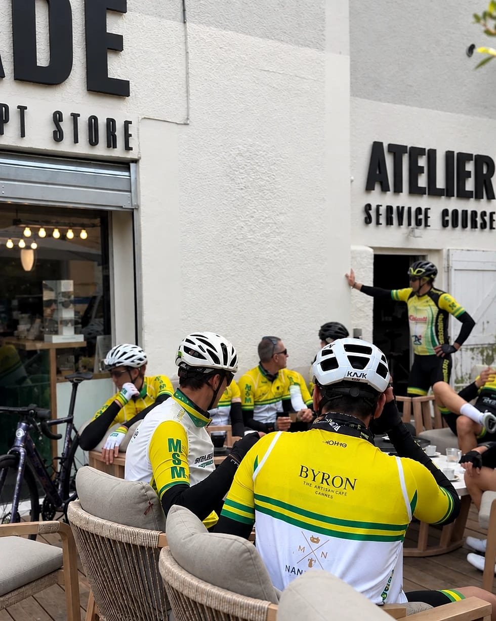 Cyclistes en maillot jaune et vert à la pause café sur la terrasse d’Escapade, devant l’atelier